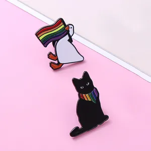 Enamel pins featuring a white goose with a rainbow flag and a black cat with a scarf