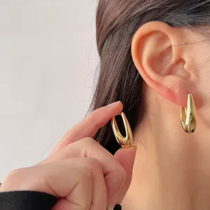 Close-up of minimalist gold water-drop hoop earrings worn on a female ear
