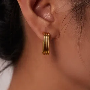 Detailed macro view of triple-layered gold U-shaped stainless steel hoop earrings on ear.