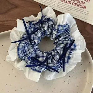 Detail view of a large blue and white plaid scrunchie with lace ruffles and bows.