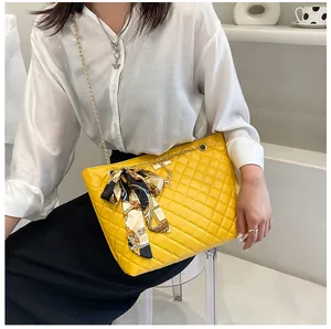 Detail view of a yellow quilted shoulder bag with a silk scarf bow and gold chain.