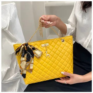 Detail view of yellow quilted shoulder bag with silk scarf bow and gold deer charm.