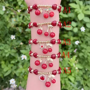 Primo piano di vari braccialetti con ciondoli a ciliegia rossa e cuore dorati