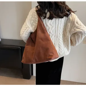 Macro view of vintage brown suede tote bag worn over a white chunky knit sweater
