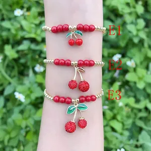Primo piano di tre braccialetti con ciliegie e perline rosse e dorate su un polso.