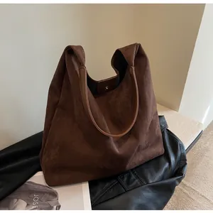 Large brown suede hobo bag with leather strap presented on a stylish black jacket.