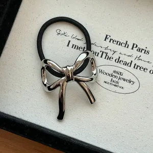Close-up of a silver metallic bow hair tie displayed on a textured fabric background