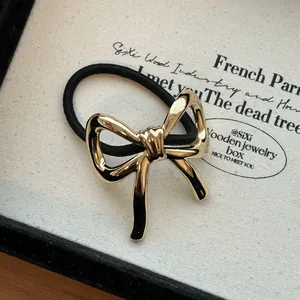 Close-up of elegant gold bow alloy hair tie with black elastic band texture detail.