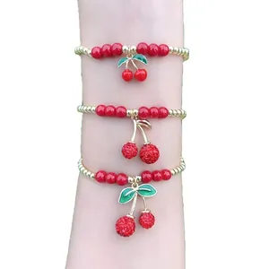 Set di tre braccialetti di perline ciliegia rossi con ciondoli placcati in oro al polso.