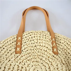 Detailed close-up view of a round straw woven beach bag with tan leather handles