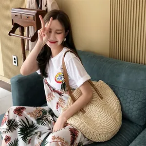 Handmade woven circular straw beach shoulder bag held by model in lifestyle setting