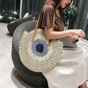 Detailed lifestyle shot of a fashionable round straw shoulder bag featuring an evil eye design