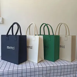 Minimalist large felt tote bags with "merci" print in multiple colors on a grid table.