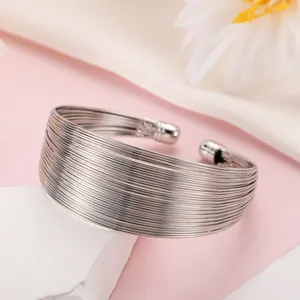 Close-up detail of silver multi-strand open cuff bracelet on elegant pink background.