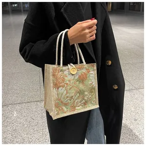 Elegant floral tapestry tote bag with rope handles held by a woman in a black coat.