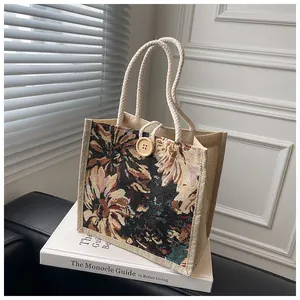 Floral tapestry tote bag with rope handles and wooden button detail shown on a white book