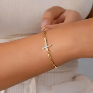 Detailed view of a golden paperclip chain bracelet with a CZ-paved sideways cross charm.