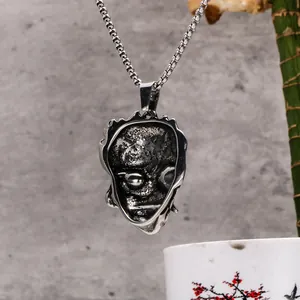 Gros plan d'un pendentif masque de démon rétro en acier inoxydable texturé.