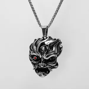 Détail d'un pendentif masque de démon vintage en acier inoxydable avec crocs et œil rouge.