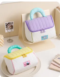 Detail of two pastel house-shaped padded makeup bags with embroidered handles and patches.