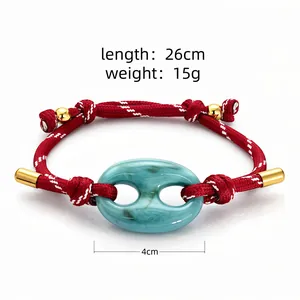 Dettaglio di un bracciale intrecciato rosso con elemento centrale in acrilico turchese.