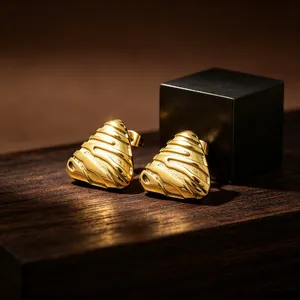 Close-up of golden triangular stud earrings with vintage embossed texture on wood.