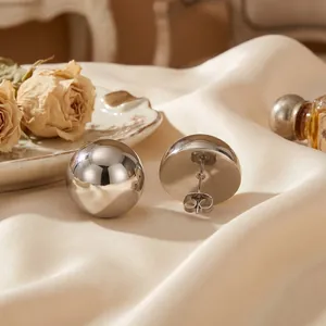 Detail shot of glossy silver stainless steel hemispherical stud earrings on silk background.