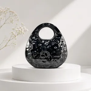 Detail of a chic black glossy hammered texture evening handbag on a white pedestal