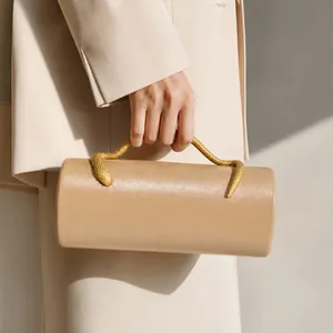 Close-up of elegant beige cylinder clutch with decorative gold snake handle