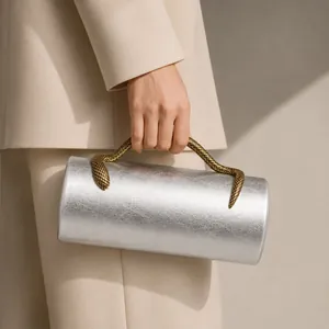 Close-up detail of a chic silver cylindrical evening clutch featuring a gold snake-shaped handle
