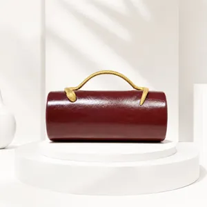 Detailed view of burgundy cylindrical evening bag with gold snake-shaped handle