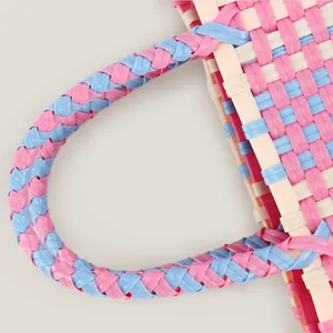 Close-up of a colorful hand-woven plastic picnic bag with braided handle details.