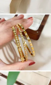 Close-up of gold titanium steel bangles with geometric zircon patterns in a box.