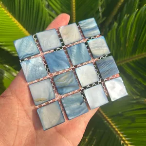 Detailed view of a hand-held square mosaic coaster made of iridescent blue natural shells