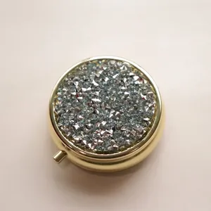 Close-up detail of a portable sparkling diamond-inlaid gold metal round pill box cover