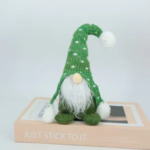 Vue détaillée d'un gnome de Noël tricoté vert assis sur un accessoire de livre.