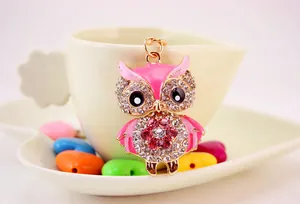 Close-up of a pink rhinestone owl keychain pendant hanging on a white teacup with colorful heart beads