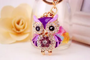 Close-up of a cute golden owl keychain decorated with purple crystals and enamel details