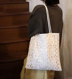 Detail of a white lace sequin embroidered tote bag carried by a model on stairs