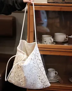 White lace tote bag with sequin embroidery shown hanging in a warm interior setting.