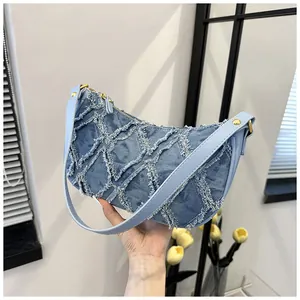 Detailed view of a denim crescent hobo bag featuring distressed fringe and light blue leather strap
