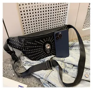 Detail of black punk waist bag with silver rivets and skull, shown next to a smartphone