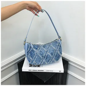 Detail of blue denim crescent bag with frayed diamond pattern on modern display