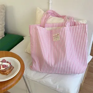 Stylish pink and white striped canvas tote bag with cute heart label detail on a cozy bed