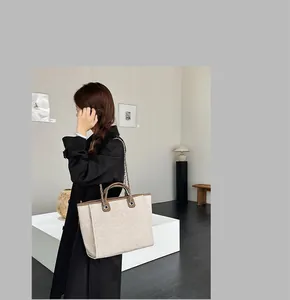 Detailed view of a large beige canvas tote bag with chain strap and brown handles