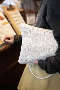 Elegant white lace sequin shoulder bag detail view held by model in cafe setting