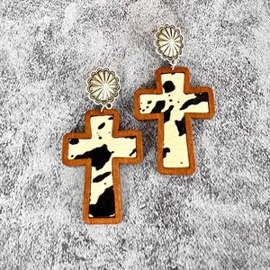 Close-up detail of western style cross earrings with wood frame and cow print leather inlay