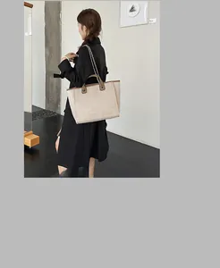 Asian model wearing a large beige canvas tote bag with chain strap and brown trim