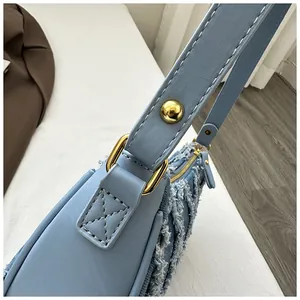 Close-up of blue denim crescent bag strap with gold buckle and white stitching detail.