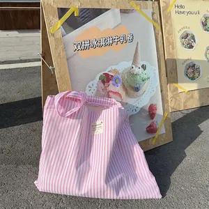 Pink and white striped canvas tote bag resting against a wooden sign in a casual setting